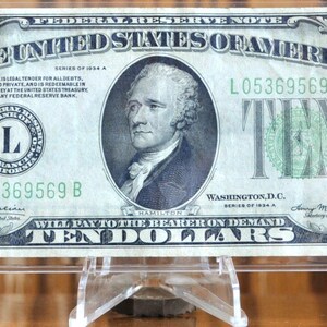 May include: A vintage 1934 A series United States ten-dollar bill featuring a portrait of Alexander Hamilton in the center. The banknote displays the text Federal Reserve Note, The United States of America, and Ten Dollars in black and green ink.
