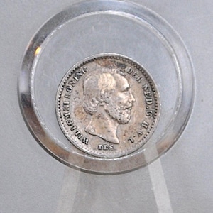May include: A silver coin with a profile of a man with a beard, surrounded by text, inside a clear, circular display case. The coin is centered in the case, which is set against a light gray background. The coin appears to be an antique.