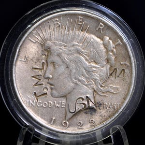 May include: A silver 1922 Peace dollar coin, displayed in a protective case. The coin features a profile of Lady Liberty with the inscription "IN GOD WE TRUST" and "LIBERTY". The year "1922" is visible. The coin is in a clear plastic holder.