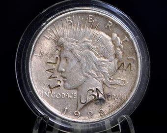 Könnte beinhalten: Eine silberne Peace Dollar Münze von 1922, in einer Schutzhülle präsentiert. Die Münze zeigt ein Profil von Lady Liberty mit der Inschrift "IN GOD WE TRUST" und "LIBERTY". Das Jahr "1922" ist sichtbar. Die Münze befindet sich in einem transparenten Kunststoffhalter.