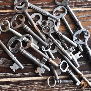 May include: A collection of antique keys with intricate designs, some with tarnished metal and others with a shiny finish, arranged on a dark wooden surface.