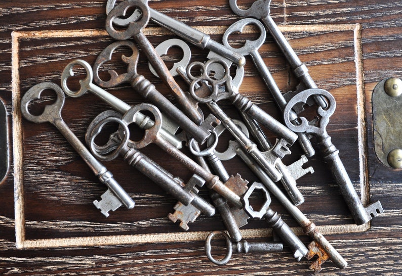May include: A collection of antique keys with intricate designs, some with tarnished metal and others with a shiny finish, arranged on a dark wooden surface.