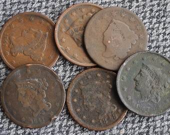 May include: A selection of antique copper coins, displaying detailed profiles and inscriptions. The coins, with visible dates, are arranged on a textured grey surface, highlighting their aged patina and historical value.