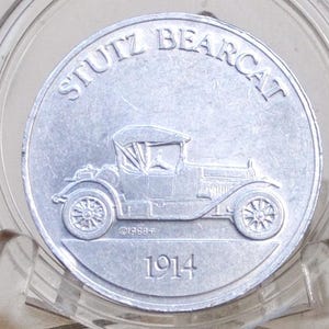 May include: A silver coin with the words "STUTZ BEARCAT" and the year "1914". The coin shows a vintage car design. The coin is presented in a clear plastic holder.