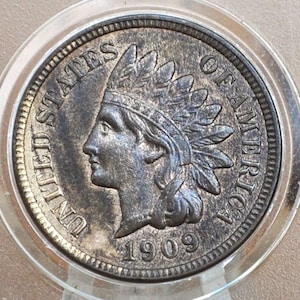 May include: A close-up of a 1909 Indian Head penny. The coin features a profile of a Native American in a feathered headdress. The words "UNITED STATES OF AMERICA" and the year "1909" are visible.