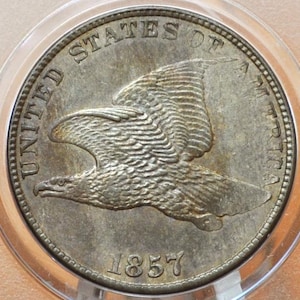 May include: A silver United States half dollar coin with an eagle in flight on the obverse. The coin is dated 1857.