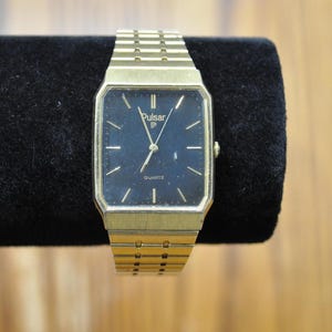 May include: A gold-tone Pulsar quartz wristwatch with a black face and a gold-tone metal strap.