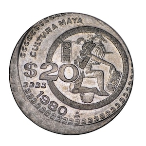 May include: A silver coin featuring a detailed relief of a Mayan figure holding a tablet, with the text "CULTURA MAYA" and "$20 1980". The coin has a circular design with intricate patterns around the edges.