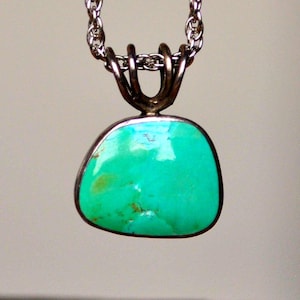 Op de afbeelding: Een zilveren hangerketting met een heldere turkooizen steen. De steen heeft een onregelmatige vorm en is gezet in een zilveren bezel. De zilveren ketting maakt de ketting compleet en creëert een elegant sieraad.