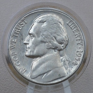May include: A silver US half dollar coin with the profile of Andrew Jackson on the obverse. The coin reads "IN GOD WE TRUST" and "LIBERTY 1954".