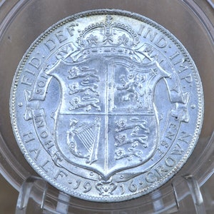 Puede incluir: Moneda de media corona de plata de 1916 con la inscripción "Georgius V Dei Gratia Britanniarum Rex et Indiae Imperator" y el escudo de armas real.