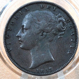 May include: A silver British penny coin with the profile of Queen Victoria and the text "VICTORIA DEI GRATIA" and "1853" on the coin.