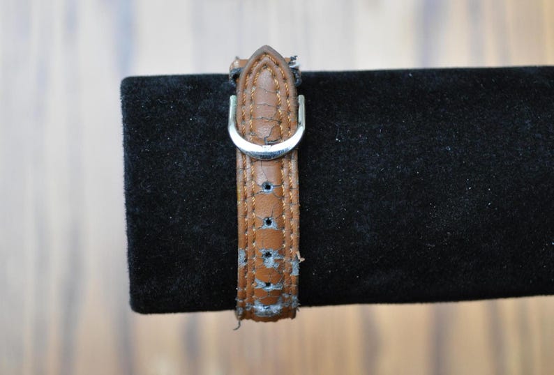 May include: A brown leather watch strap with a silver buckle. The strap has a worn look and is showing signs of age.