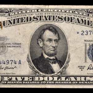 以下が含まれることがあります： アメリカ合衆国の5ドル銀貨証明書。エイブラハム・リンカーンの肖像と複雑なボーダーデザインが特徴です。「FIVE DOLLARS」と「IN SILVER PAYABLE TO THE BEARER ON DEMAND」の文字が含まれています。