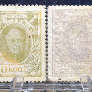 May include: Two vintage postage stamps. The first stamp features a portrait within an oval frame, with text in Cyrillic and the value "20 коп." The second stamp is blank. Both stamps are in a clear protective holder.