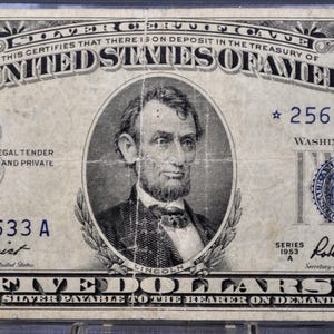 May include: A vintage five-dollar silver certificate from the United States of America. The bill features a portrait of Abraham Lincoln and the text "FIVE DOLLARS" in a decorative font. The bill is in shades of gray and green.