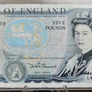 May include: A Bank of England five-pound note featuring a portrait of Queen Elizabeth II. The note has a blue and white color scheme, with text that reads "Bank of England" and "Five Pounds". The serial number is LW66 319272.