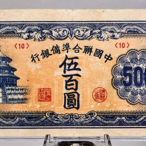 May include: An antique 500-unit banknote featuring a blue and gold design. The note displays a detailed illustration of a building, along with Chinese characters and the number 500 in multiple locations.