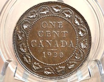 May include: A copper-colored Canadian one-cent coin from 1920. The coin features a wreath of leaves around the edge and the words "ONE CENT CANADA" in the center.