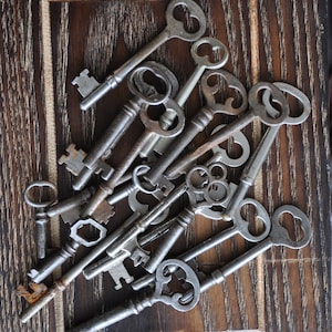 May include: A collection of antique keys in various sizes and shapes, with intricate designs and worn metal finishes. The keys are arranged on a dark wooden surface.
