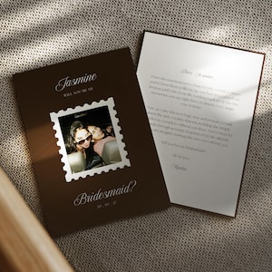 May include: A dark brown rectangular card featuring the name Jasmine, the text Will you be my bridesmaid?, and a square photo with a white postage stamp border. A second white card with black printed text is partially tucked behind the first card.