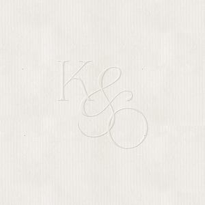 Puede incluir: Papel color crema con las iniciales en relieve "KS" en una escritura delicada y elegante. Las letras están en una fuente serif, con la "S" con un diseño cursivo y fluido. El papel tiene una superficie sutilmente texturizada.