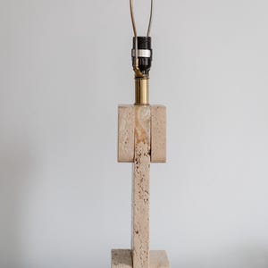 Puede incluir: Una l&aacute;mpara de mesa de travertino beige con base de lat&oacute;n y una pantalla de metal simple.
