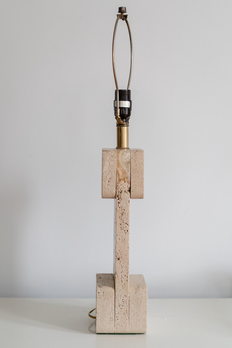 Puede incluir: Una l&aacute;mpara de mesa de travertino beige con base de lat&oacute;n y una pantalla de metal simple.