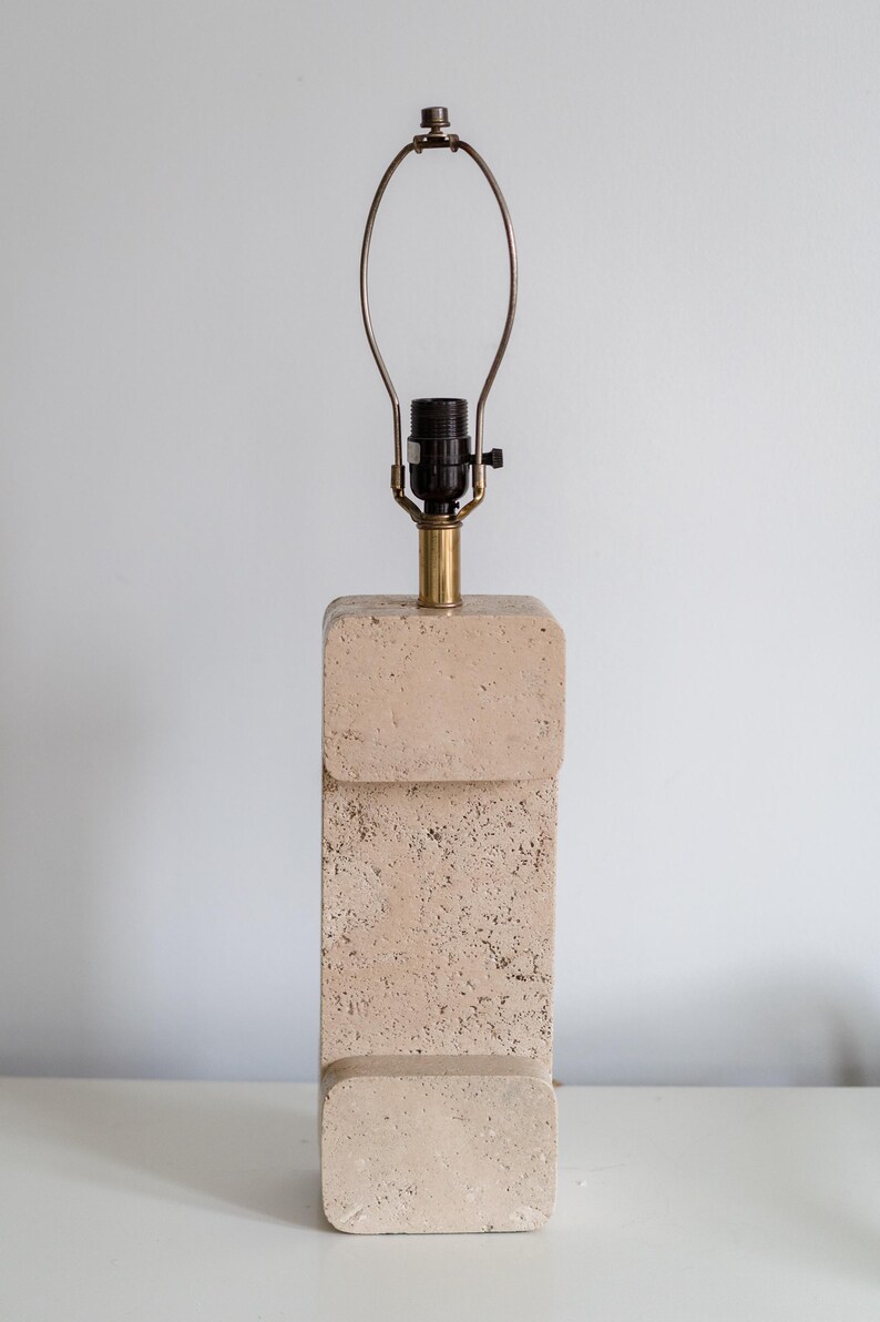 Puede incluir: Una l&aacute;mpara de mesa de travertino beige con base de lat&oacute;n y una pantalla de metal simple.