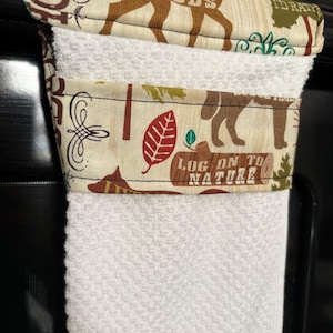 May include: A white kitchen towel with a decorative fabric band featuring a woodland theme. The band displays brown deer, red leaves, and the text "LOG ON TO NATURE" and "THROUGH THE WOODS".