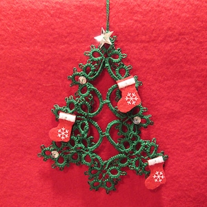 May include: A green lace Christmas tree ornament with a silver star on top and red felt stockings with white snowflakes hanging from the branches.