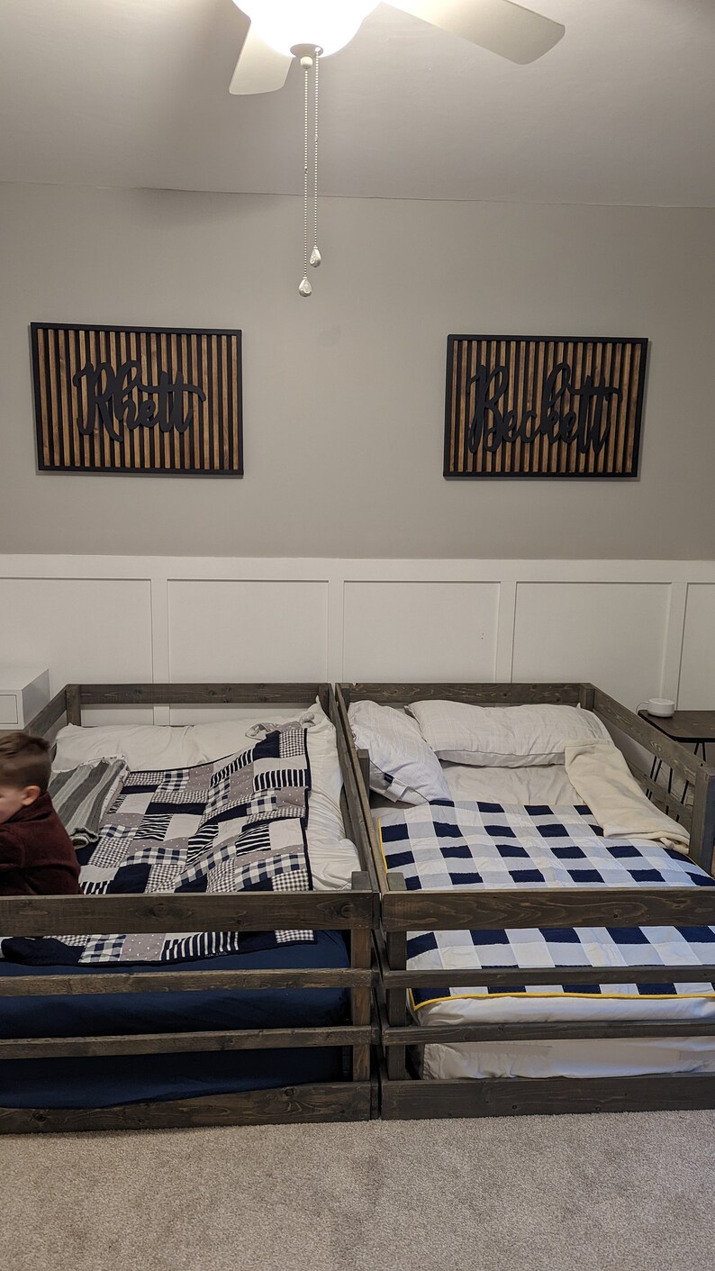 May include: Two wooden twin-sized beds with black and white checked quilts. The beds have a wooden railing around the perimeter. The beds are in a room with white walls and a ceiling fan.