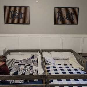 May include: Two wooden twin-sized beds with black and white checkered quilts. The beds have a wooden railing around the perimeter. The beds are in a room with white walls and a ceiling fan.
