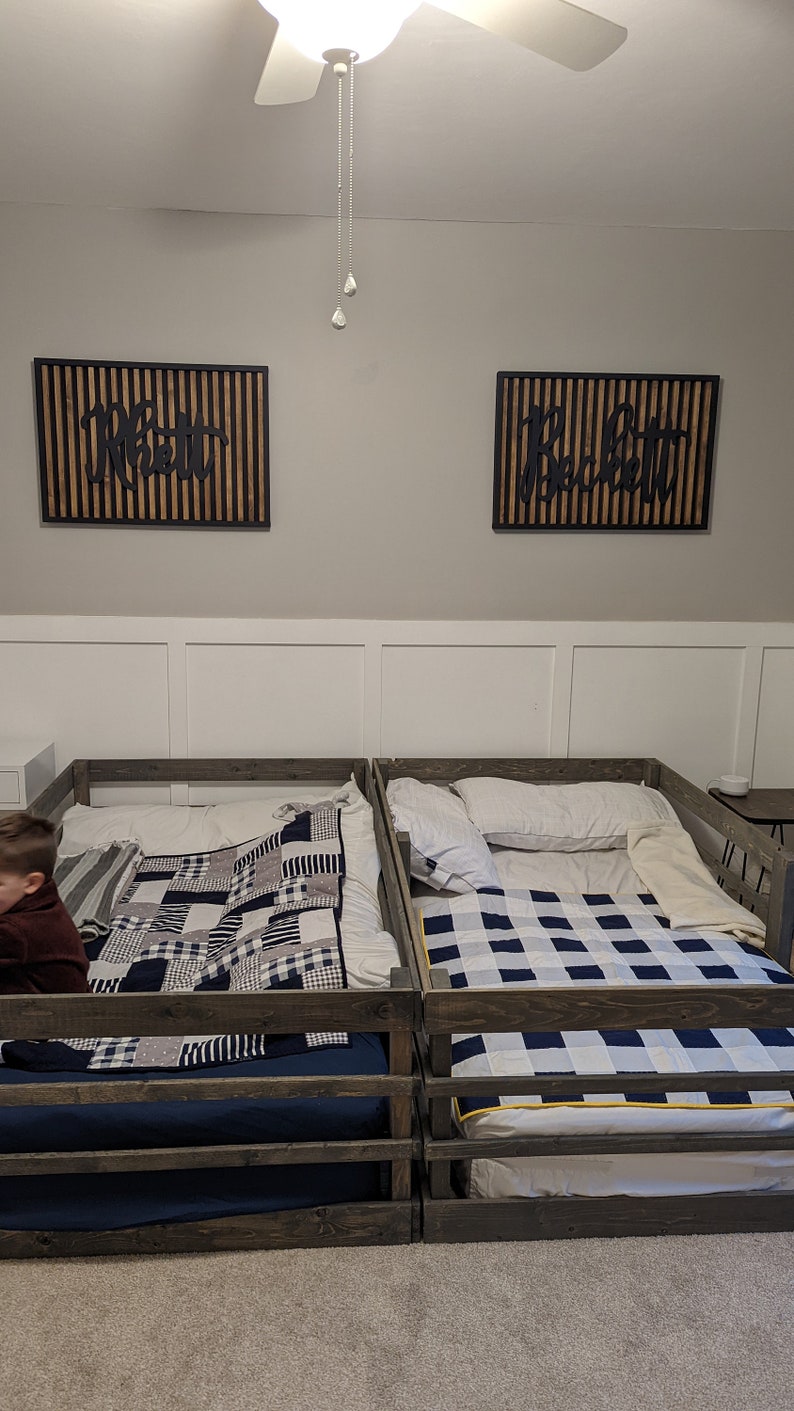 May include: Two wooden twin-sized beds with black and white checkered quilts. The beds have a wooden railing around the perimeter. The beds are in a room with white walls and a ceiling fan.