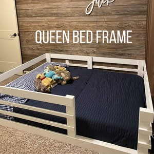 May include: White wooden queen-sized bed frame with a blue and white checkered patterned sheet and a navy blue blanket. The bed frame has a white wooden railing around the perimeter.