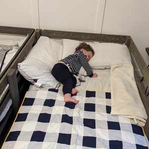 May include: A child is sleeping on a bed with a white and blue checkered quilt. The bed has a wooden frame and a white pillow.