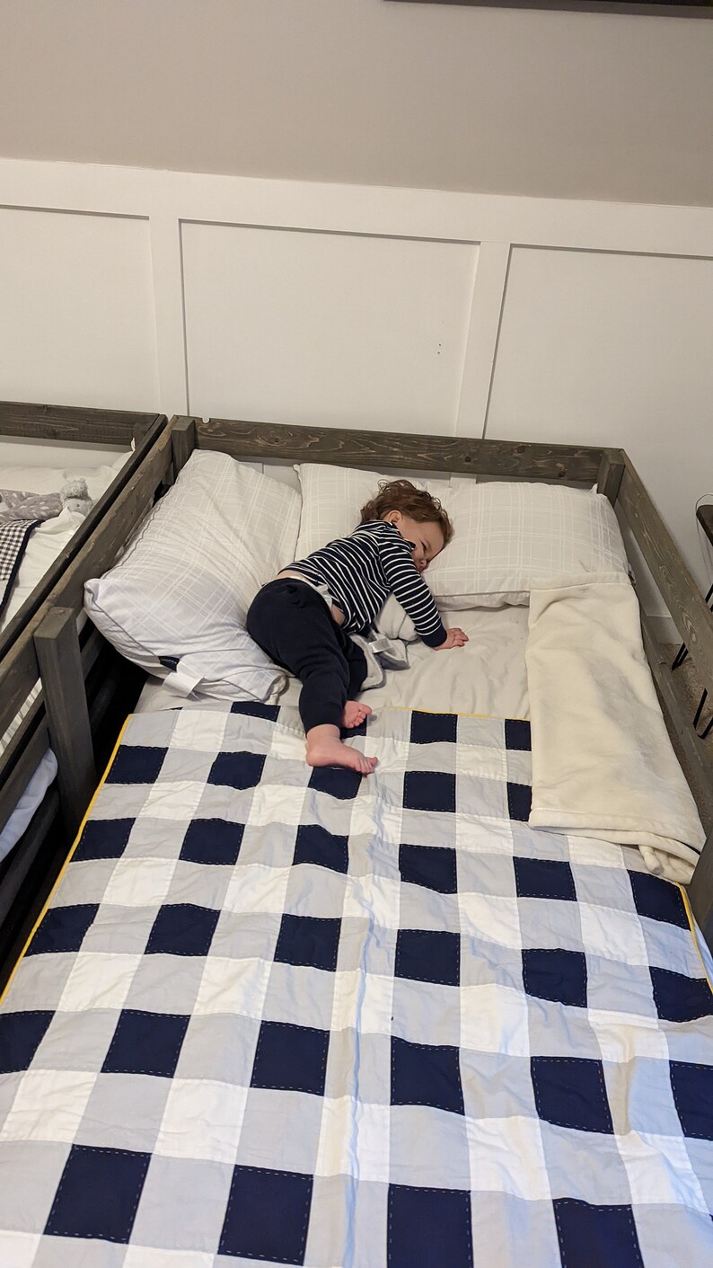May include: A child is sleeping on a bed with a white and blue checkered quilt. The bed has a wooden frame and a white pillow.