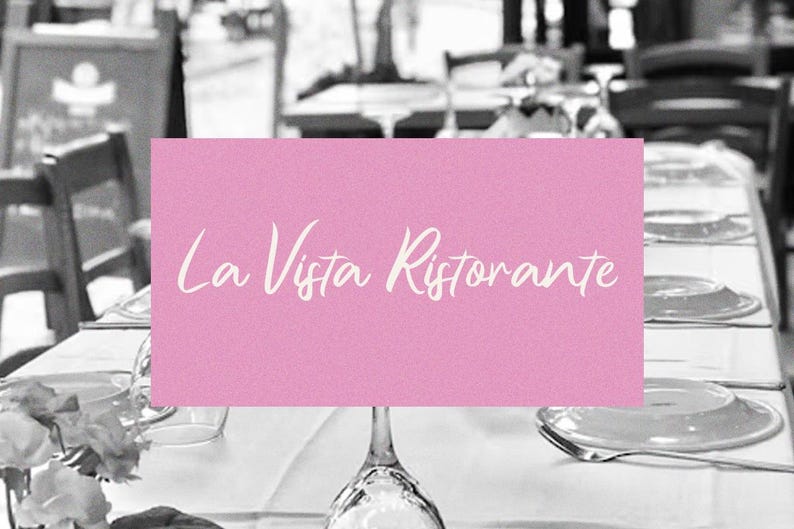 May include: A pink sign with white text that reads "La Vista Ristorante" on a table set with white linens and silverware in a restaurant.