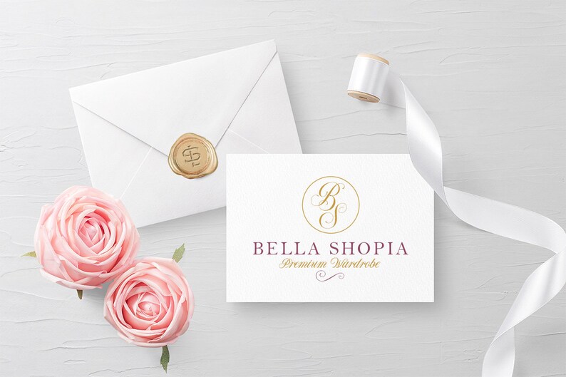 May include: A white card with a gold circle containing the letters "B" and "S" in a cursive font. The text "BELLA SHOPIA Premium Wardrobe" is below the circle in a burgundy font.