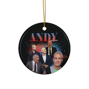 Puede incluir: Adorno redondo de cerámica con fondo negro que presenta múltiples imágenes de Andy Cohen. El texto "ANDY Cohen" está en rojo y dorado. Se adjunta un cordón dorado para colgar.
