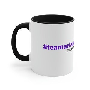 Könnte beinhalten: Weiße Keramik-Kaffeetasse mit schwarzem Rand und Henkel. Die Tasse hat einen lila Hashtag mit der Aufschrift "#teamarian" und einen kleineren Hashtag mit der Aufschrift "#scandal".