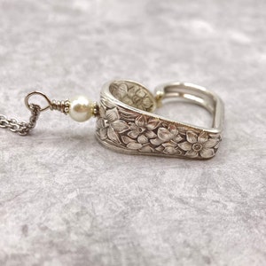 May include: A silver heart-shaped pendant necklace with a floral design and a single pearl bead.