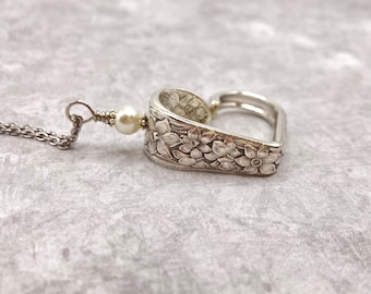 May include: A silver heart-shaped pendant necklace with a floral design and a single pearl bead.