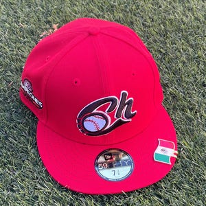 May include: A red baseball cap with a curved brim. The cap features a stylized "6h" logo with a baseball, a pin with a flag, and the text "Campeones". The cap size is 7 3/8.