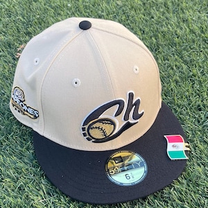 May include: Tan baseball cap with a black brim. The cap features the letters "Ch" with a baseball graphic, a "Campeones" patch, and a pin with a flag design. The cap size is 6 7/8.