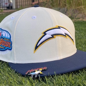 May include: Cream-colored baseball cap with a navy blue brim. Features a team logo and a "Pro Bowl 2004 Hawaii" patch. A pin of a cartoon character is on the brim.