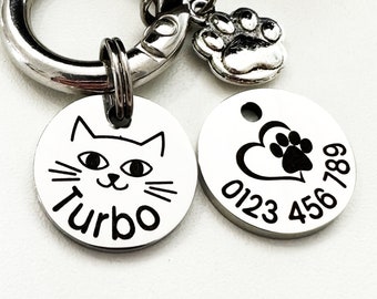 May include: Silver pet ID tag with a black cat face and the name "Turbo" engraved on one side and a black heart with a paw print and the phone number "0123 456 789" on the other side. The tag is attached to a silver split ring.
