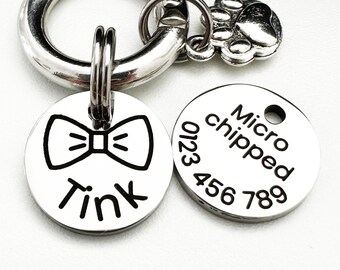May include: Silver dog tag with a black bow tie and the name "Tink" engraved on it. A second silver tag is engraved with "Micro chipped" and the number "0123 456 789".