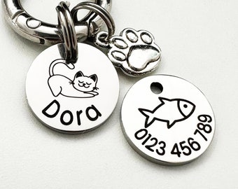 May include: Silver pet ID tag with a paw print charm, a round tag with a sleeping cat and the name "Dora" engraved, and a round tag with a fish and the phone number "0123 456 789" engraved.