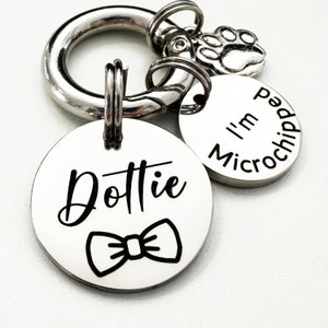 May include: Silver dog tag with the name "Dottie" engraved on it, a black bow tie design, and a smaller silver tag that says "I'm Microchipped".